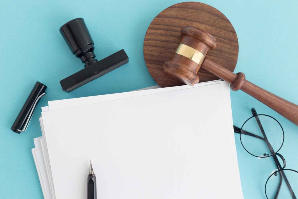 A gavel, a stamp, and a pen rest on a stack of paper.